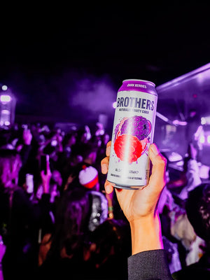 A can of Brothers Dark Berries being held up in a festival crowd