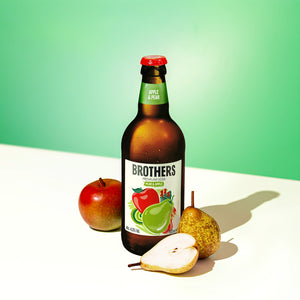 Brothers Apple & Pear cider bottle with an apple and pear on a light surface and green background