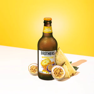 Brothers Pineapple & Passionfruit cider bottle with fresh fruit on a yellow background