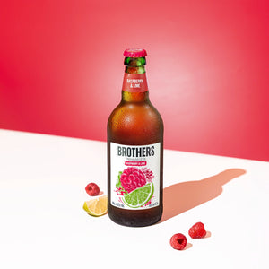Brothers Raspberry & Lime cider bottle with raspberry and lime slices on a white surface against a red background