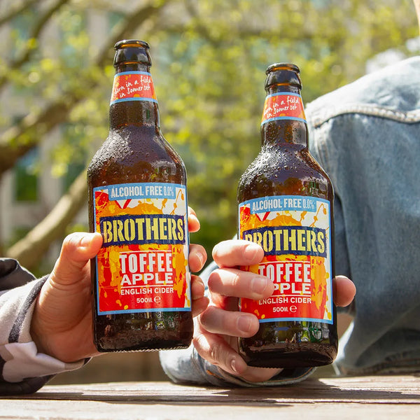 Two people enjoying Brothers Alcohol-Free Toffee Apple fruit cider outdoors