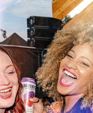 Two women laughing with a Brother's can at an outdoor event.
